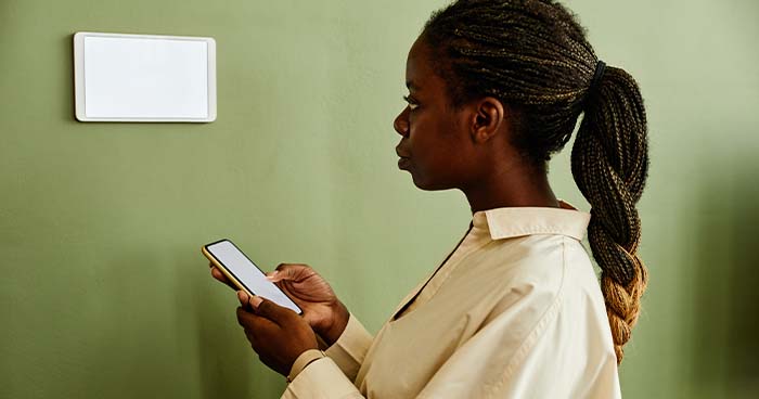 Woman Checks Her Smartphone And Smart Thermostat.