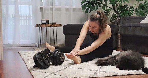 Image: A Woman Stretching With Her Cat Before A Workout In Her Home Gym.