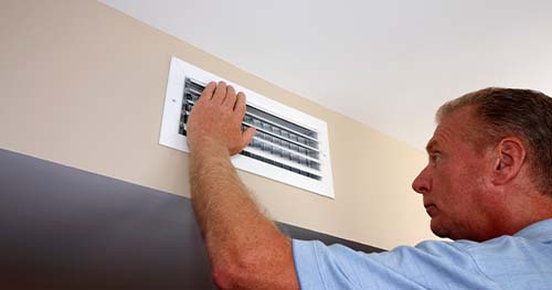 Image: A man stares into his air vents, wondering why they don't work and why his heating bill is so high.