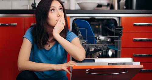 Image: A woman sits despondently next to a broken dishwasher.